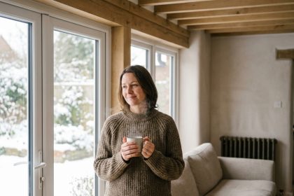 Femme confortable près d'une nouvelle fenêtre double vitrage en hiver, illustrant les économies de chauffage